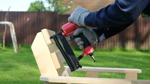 Carpenter using a red pneumatic nail gun to assemble a wooden deck chair ar.. Stock Photos