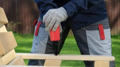 Carpenter using a red pneumatic nail gun to assemble a wooden deck chair ar.. Stock Photos