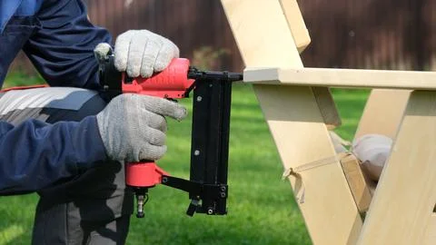 Carpenter using a red pneumatic nail gun to assemble a wooden deck chair ar.. Stock Photos