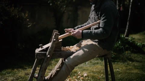 Carpenter using shave horse and draw knife to carve log into cross Stock Footage 271190147