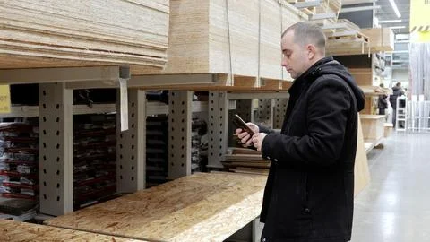 Carpenter using a smartphone while selecting wood materials for construction in 写真素材