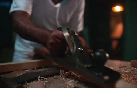 Carpenter using wooden hand plane tool to shape wooden plank Stock Footage 295605885