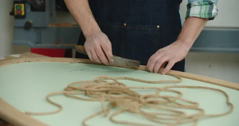 A carpenter wearing working with a hammer and nails. Nails a rope to a wooden Stock Footage 170321374