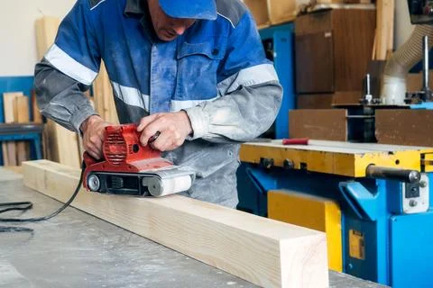 Carpenter in work clothes processes wood with grinder. Polishing of wood surface Stock Photos