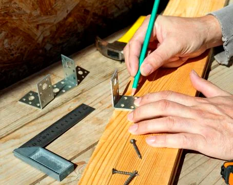Carpenter at work. Makes a mark before screwing the corner to the wooden plank. Stock Photos