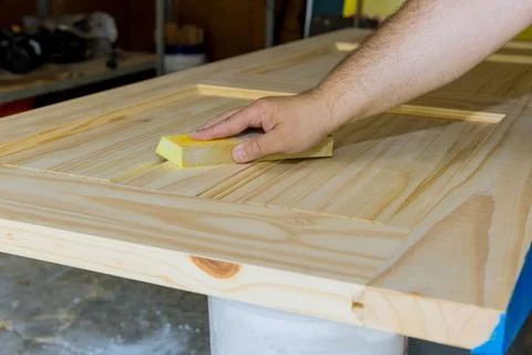 Carpenter in work on worker sanding with sanding block wooden door Stock Photos