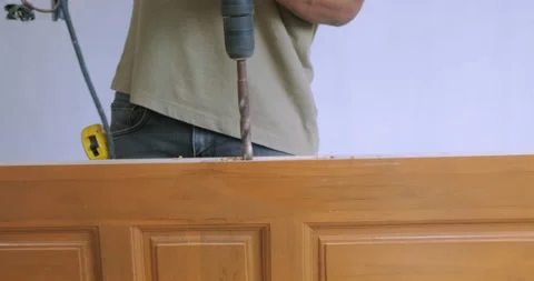 Carpenter working drill on wooden teak door set up interior house Stock Footage 153205343