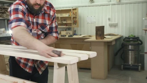 Carpenter working in a shirt with a beard in the workshop heats a wooden bench Stock Footage 88996454