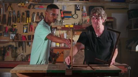 Carpenter working at workshop with the help of apprentice, small business w.. Stock Photos