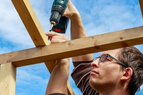 The carpenter wraps a self-tapping screw with an electric screwdriver Stock Photos
