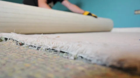 Carpenter in yellow protective gloves rolling old carpet in roll during home Vidéo 318992588