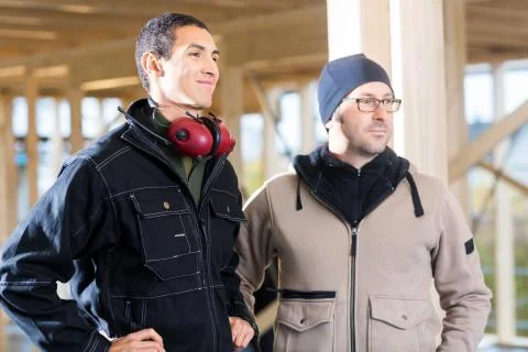 Carpenters In Jackets Looking Away While Standing At Site Stock Photos
