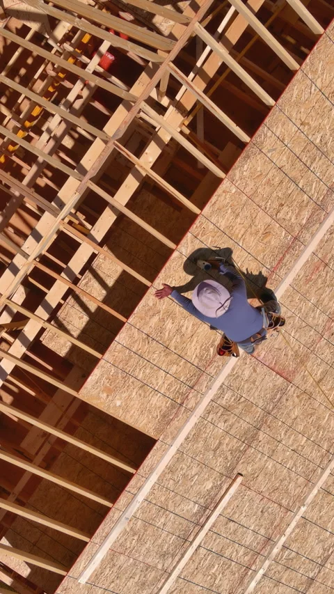 Carpentry construction workers hammer nails into plywood on roof top of a future Stock Footage 258775715