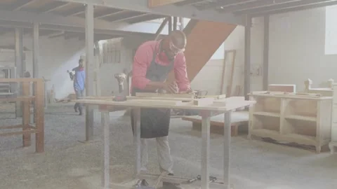 Carpentry worker measuring, planing plank at bench with helpers arriving holding Stock Footage 334120580