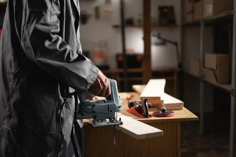 Carpentry workshop concept. Elderly Carpenter sawing plywood sheet with ele.. Stock Photos