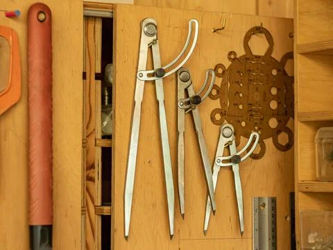Carpentry workshop. Three iron compasses of different sizes hang on the door  Stock Photos
