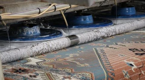 Carpet cleaning machine with rotating brushes spraying water over patterned rug Stock Photos