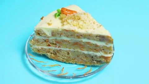 Carrot cake slice on a blue background showing creamy frosting, walnuts, and Stock Footage 321533061