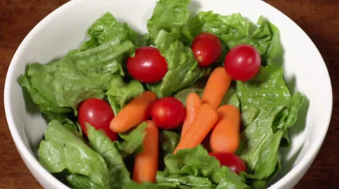 Carrots and cherry tomatoes fall in slow motion atop lettuce to create a salad. 스톡 동영상 34660456