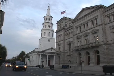 Cars drive by a white church with a tall steeple and a government building. Stock Footage