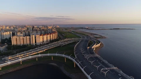 Cars going on multi-level road junction on the sea shore with city buildings on Stock Footage 92332696