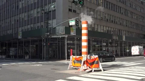 Cars pass an orange & white hot steam pipe in a road, Manhattan, New York. Stock Footage