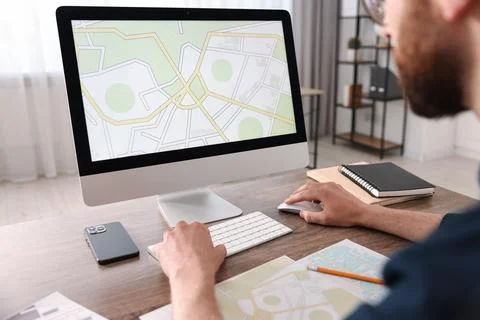 Cartographer working with cadastral map on computer at wooden table in offi.. Fotos de archivo