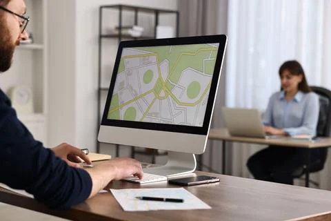 Cartographer working with cadastral map on computer at wooden table in offi.. Fotos de archivo