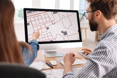 Cartographers working with cadastral map on computer at table in office, ba.. Fotos de archivo