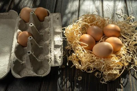 A carton holds three eggs while five more are placed in straw nearby. Sunli.. Stock Photos