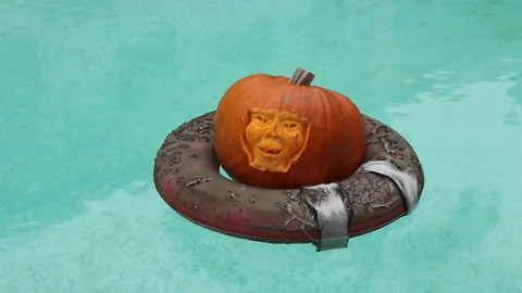 A carved face pumpkin Jack-o-lantern floating on a decayed life ring in a pool 스톡 동영상 158335370