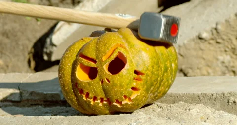 A carved orange pumpkin gets smashed with a giant hammer Video stock 145054547