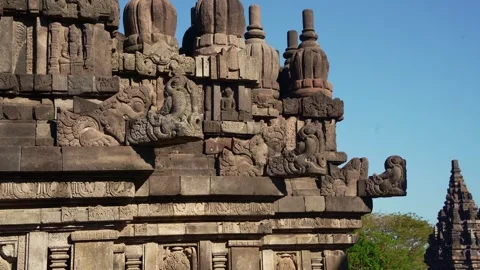 Carved temple wall leads toward a distant Prambanan spire under brilliant t.. Stock Footage 341544014