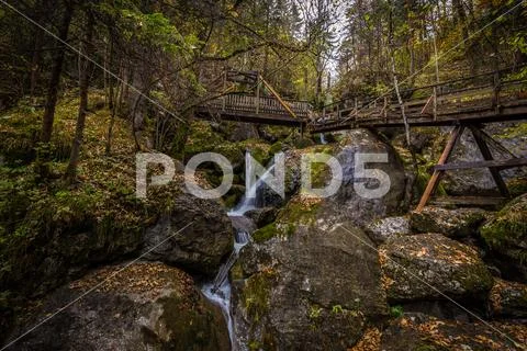 Cascade falls over mossy rocks with wooden bridge over the waterfall Stock Photos