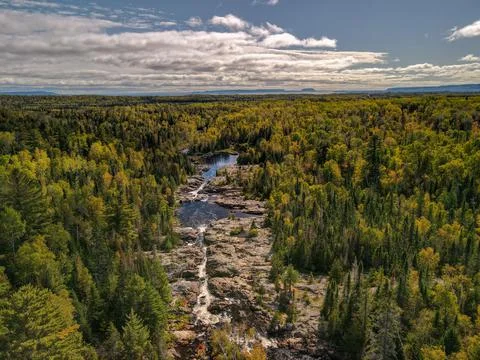 Cascade river rocks through forest with lake and mountain background Stock Photos