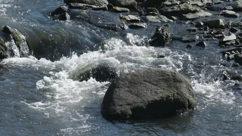 A cascade of water flows down over riverbed rocks in this stream. 4K tripod Stock Footage 141210556