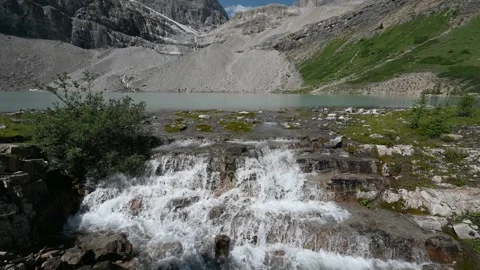 Cascading small waterfall and a calm mountain lake with green colored water Stock Footage 306479362