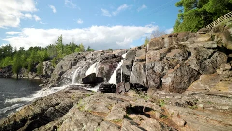 Cascading waterfall flows down rock face into lake basin on bright sunny 動画素材 196918011