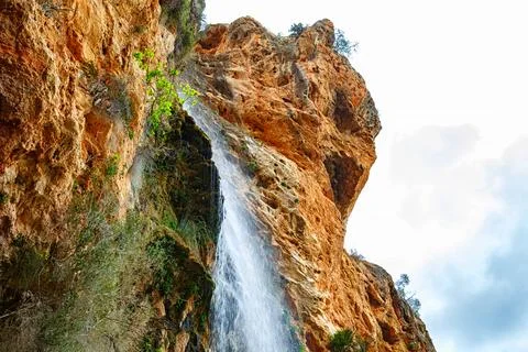 A Cascading Waterfall Flows Down a Rocky Cliff Surrounded by Lush Greenery .. Stock Photos