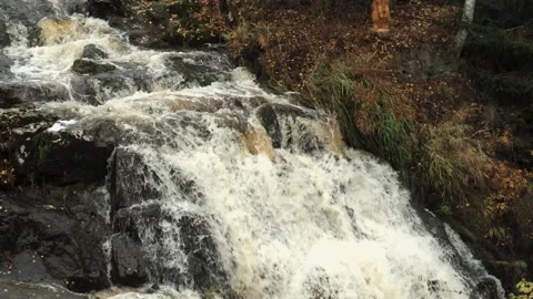Cascading waterfall flows over rocky terrain, surrounded by autumn foliage Stock Footage 319963247