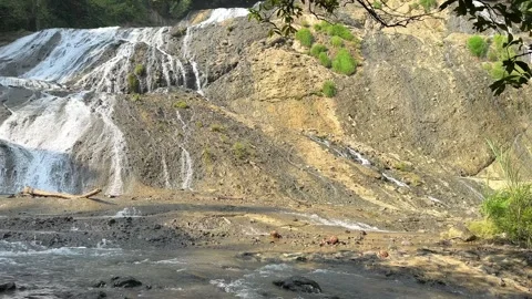 Cascading Waterfall Over Rocky Cliffs, Lush Green Jungle, Wide Static Shot Video stock 325303996