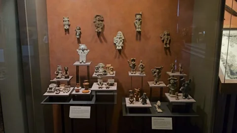 Case of Small Clay Figurines Against Orange Museum Wall, Mexico 8K Stock Footage 340369419