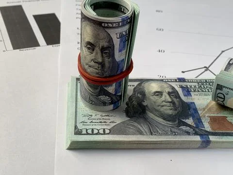 Cash bundles and a rolled stack of hundred-dollar bills rest on financial Stock Photos