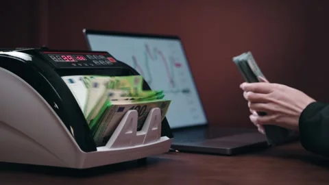 Cash counting machine processes banknotes while a person types on a laptop, Stock Footage 331080380