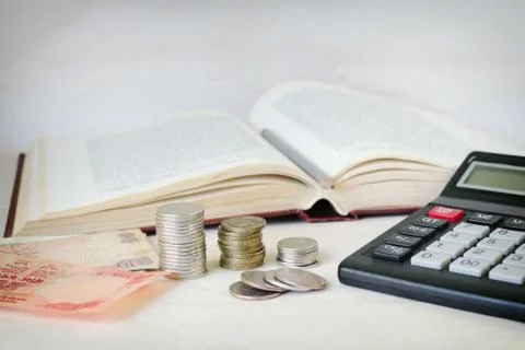 Cash notes, stacks of coins and a calculator in front of an open book. Stock Photos