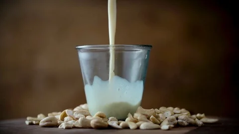 Cashew Milk pouring into glass with cashews rotating Stock Footage