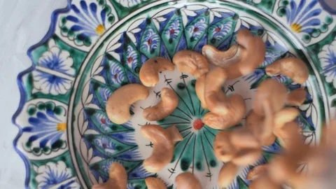 Cashew nuts falling on the oriental plate with blue and white pattern Stock Footage 128301757