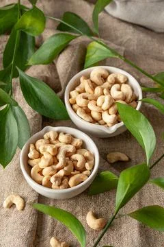 Cashew nuts in two white cups. Fabric background. Nearby cashews and green le Stock Photos