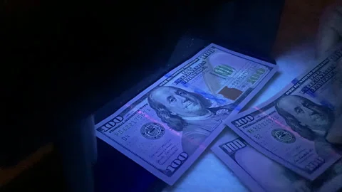 Cashier checking 100 dollar bills under uv light Stock Footage 297203005