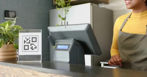 Cashier using POS terminal in cafe gesturing at QR code as customer scanning Vídeo Stock 335986404